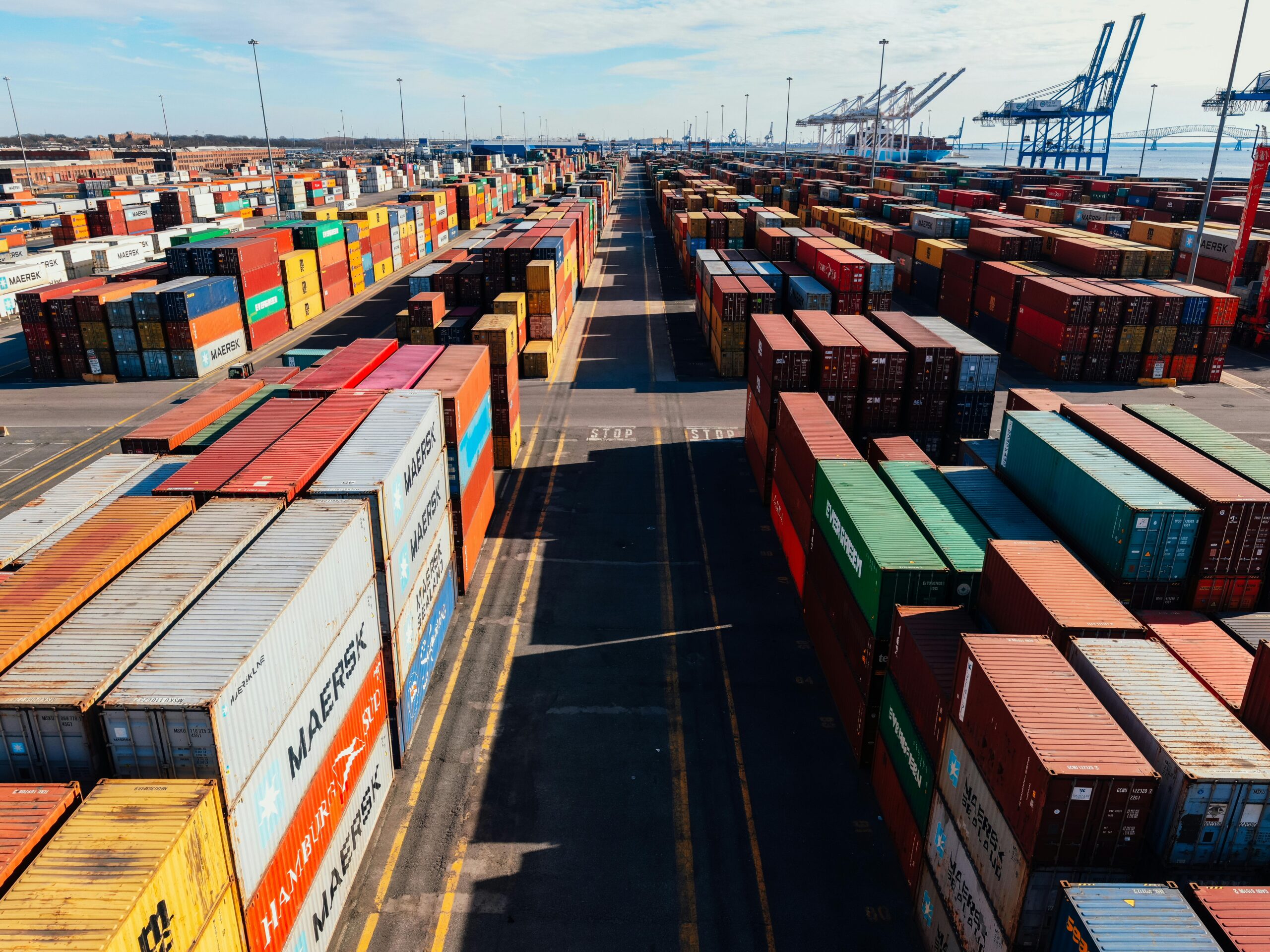 From above of asphalt roadway among large colorful metal containers placed in industrial area under cloudy sky in sunny day
